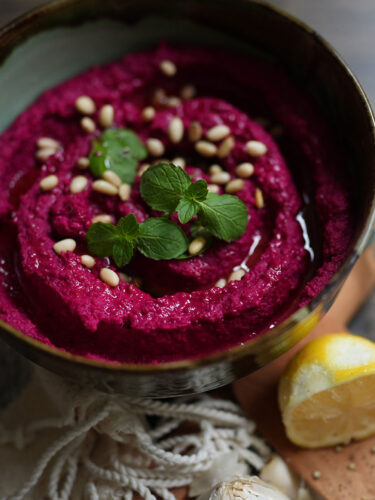 A creamy, bright creamy bowl of Easy Beet Hummus garnished with sesame seeds and parsley