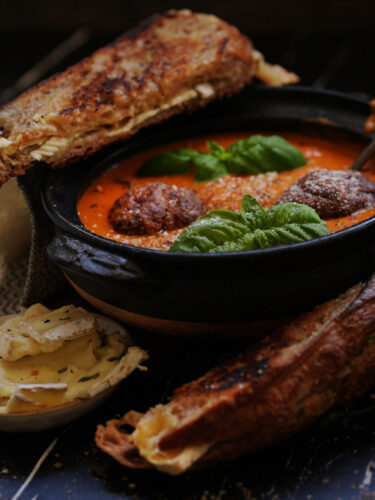 A warm bowl of homemade tomato soup with sourdough croutons and fresh basil, served with a side of golden sourdough grilled cheese