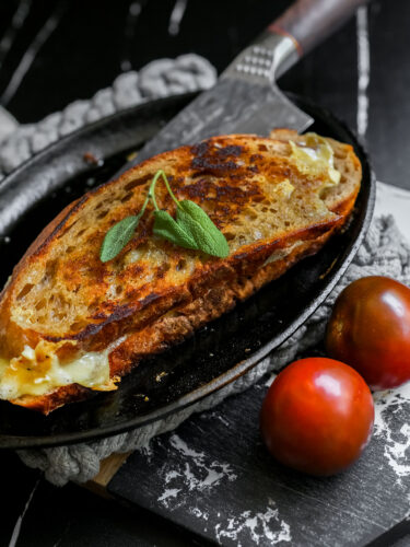 Sourdough grilled cheese in a cast iron skillet with fresh tomatoes and a knife beside it—crispy, golden, and ready to serve.