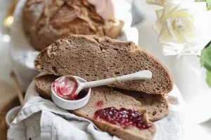 Half of a Golden Crumb sourdough loaf showing the crumb, with a spoonful of jelly on a slice of bread and a small dish beside it