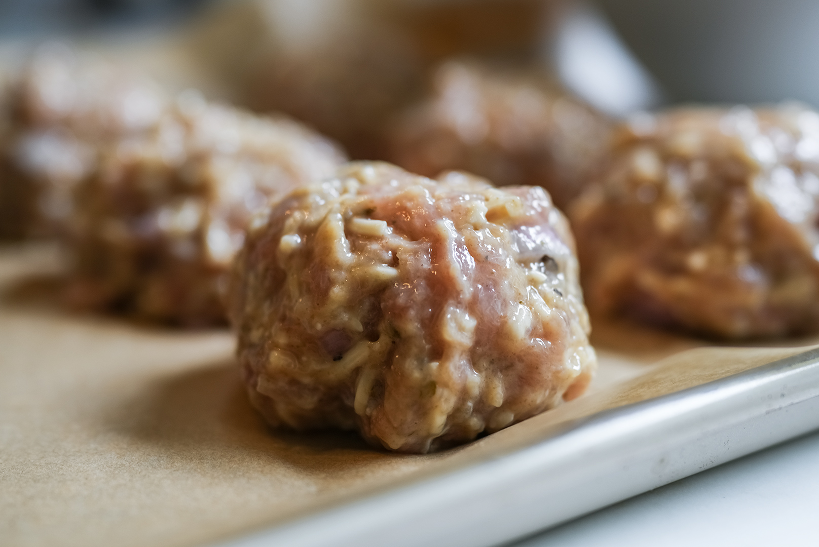 Oven baked sourdough discard chicken meatballs golden olive oil brushed over a sourdough discard chicken meatball highlighting its texture before baking A rustic close up view of high protein meatballs prepared for the oven with sourdough starter magic Sourdough afterglow Close-up of oiled sourdough discard chicken meatball on a baking sheet, ready for oven baking, with other meatballs blurred in the background