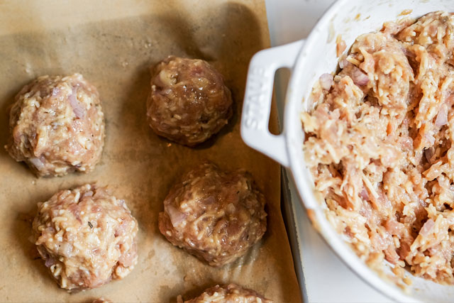 Oven baked turkey meatballs sourdough afterglow recipe sourdough afterglow Staub bowl filled with raw turkey meatball ingredients beside a parchment-lined baking sheet of shaped turkey meatballs