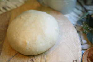Round ball of sourdough dough resting on a rustic wooden board before going into the cold proof stage