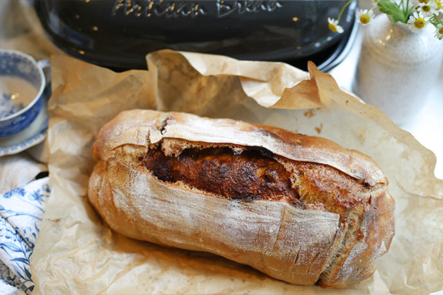 Afterglow swirls cinnamon sourdough bread with brown sugar s a golden cinnamon swirl sourdough loaf cools on the counter after being baked in an emile henry artisan baker a soft daisy adds a gentle touch while the baker watches quietly in the background a peaceful pause before slicing into something sweet and slow fermented sourdough afterglow cinnamon-swirl-sourdough-loaf-emile-henry-baker-daisy