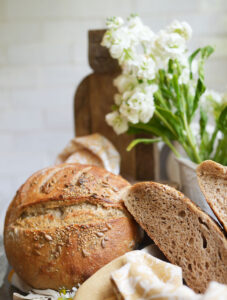 Crispy seeded sourdough with two crumb halves to the right and flowers in the background