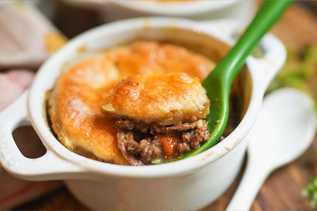 Sourdough beef pot pie in white cocottes flaky crust comfort the first bite of a mini sourdough beef pot pie balanced on a green spoonflaky crust giving way to savory filling A comforting cozy moment captured just before it disappears Sourdough afterglow A flaky bite of sourdough beef pot pie resting on a green spoon, the first scoop revealing tender filling beneath the golden crust