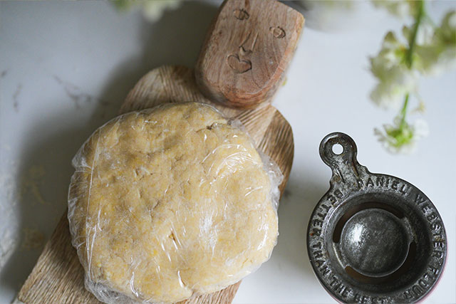 Sourdough beef pot pie in white cocottes flaky crust comfort sourdough pie dough wrapped in plastic wrap and resting on a wooden board ready for the fridge A happy face drawn into the dough adds a playful cozy touch Sourdough afterglow Rolled sourdough dough wrapped in plastic with happy face on wooden board