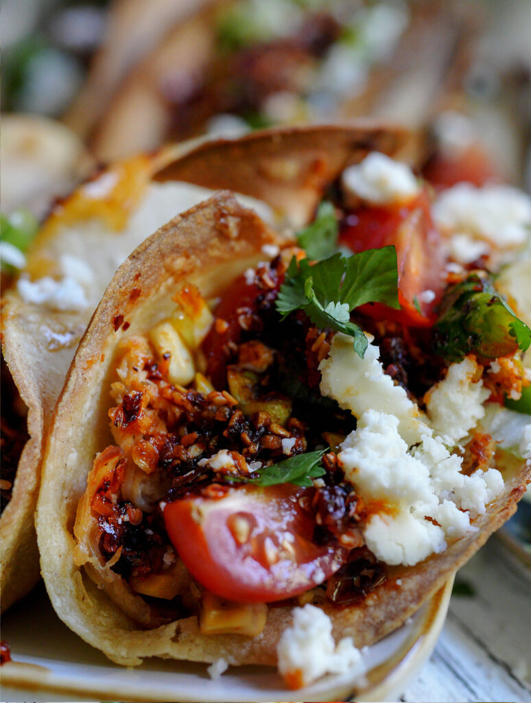 Crispy chicken taco topped with corn salsa, chili crunch, cotija cheese, tomato, and fresh cilantro