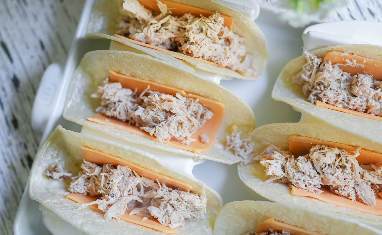 Crispy chicken tacos with corn salsa corn tortillas with slices of american cheese are filled with juicy beer simmered shredded chicken and arranged in a taco rack This step sets up the crispy baked tacos before they go in the oven Sourdough afterglow Corn tortillas layered with American cheese and filled with shredded chicken, nestled in a taco rack ready for baking