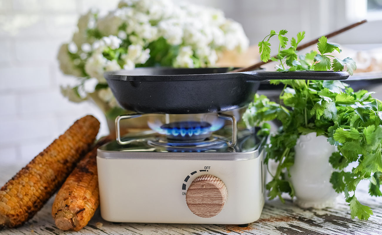 Crispy chicken tacos with corn salsa grilled corn cobs rest beside a burner top skillet with fresh cilantro spilling from a white pitcher nearby A rustic kitchen moment capturing the prep for the creamy corn salsa in the crispy chicken tacos recipe Sourdough afterglow Grilled corn next to a cast iron skillet on a stovetop burner with fresh cilantro in a white pitcher—ingredients for coconut corn salsa