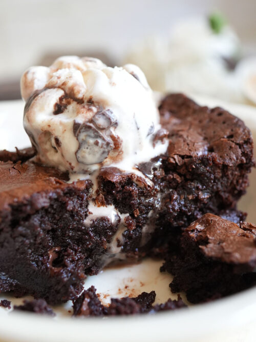 Close-up fudgy brownie topped with a scoop of vanilla swirl ice cream, chocolate sauce dripping down the sides
