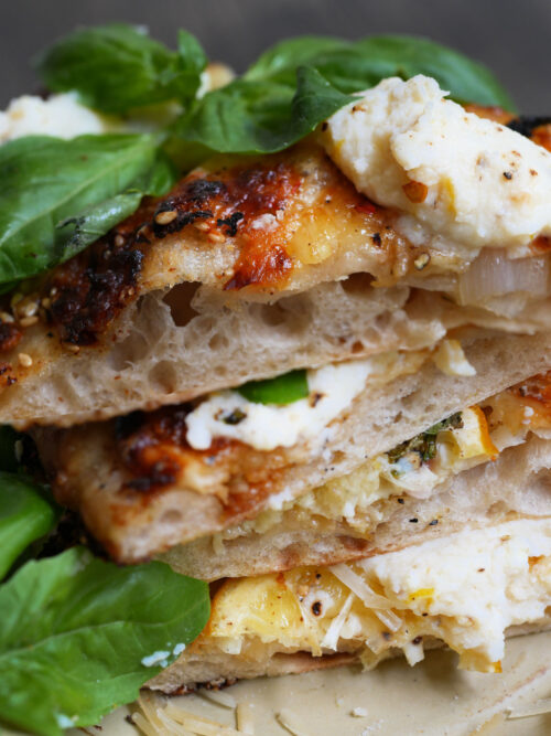 Stacked slices of lemon ricotta sourdough pizza topped with fresh basil leaves on a golden crust.