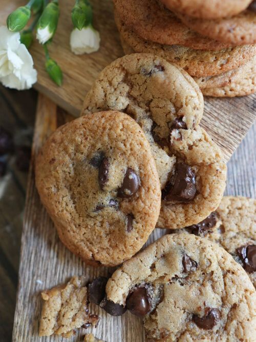Stack of Salted Butter Sourdough Discard Chocolate Chip Cookies on a rustic wooden board, with golden edges and gooey chocolate chunks in warm natural light.