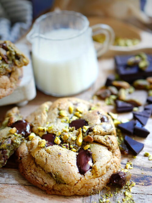 Close-up of gooey Pistachio Sourdough Chocolate chip Cookies with melted chocolate chunks and crushed pistachios, served with milk.