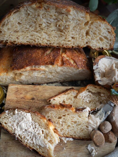 Rustic apple cider and maple sourdough bread on a wooden board, slices buttered with cinnamon maple nutmeg whipped butter, cider drizzle soaking the crust.