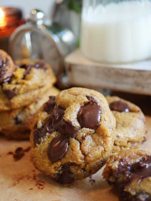Close up of sourdough pumpkin spice chocolate chip cookies with melted chocolate chunks, stacked with a glass of milk in the background.