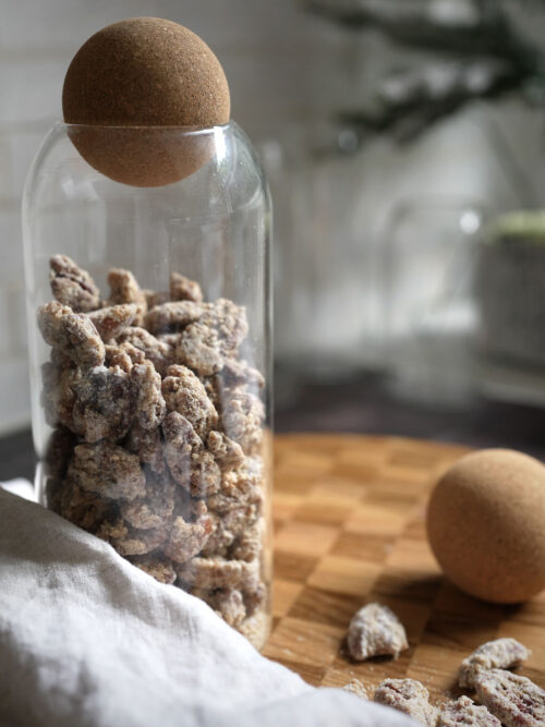 Jar of candied tahini pecans with a cork lid on a wooden board with linen in soft natural kitchen light