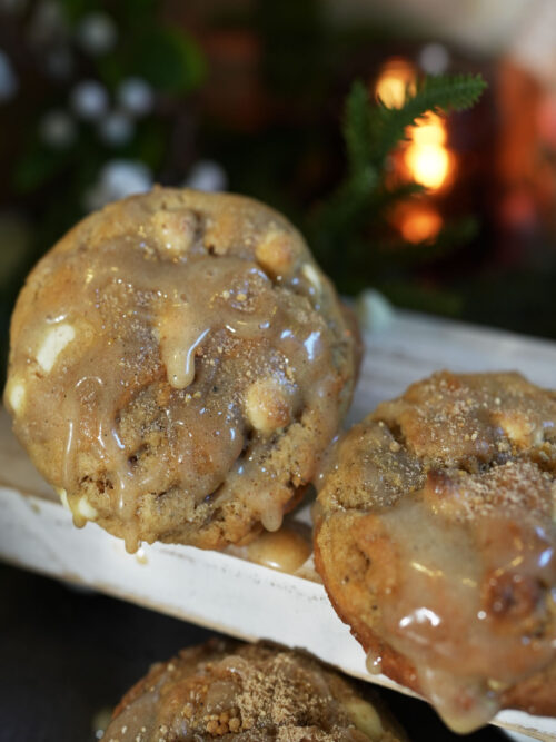Tahini sourdough cookies drizzled with maple glaze and sprinkled with cinnamon sugar on a white board with soft candlelight and greenery in the background.