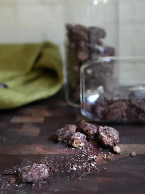 Espresso maple sourdough candied pecans with dark chocolate and flaky sea salt on a wooden board with glass jars